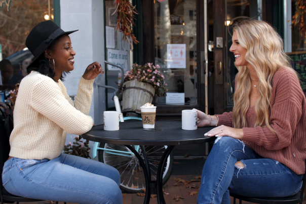 Two girls having coffee outside a shop, Fall leaves on the ground, girls are dressed in fall sweaters
